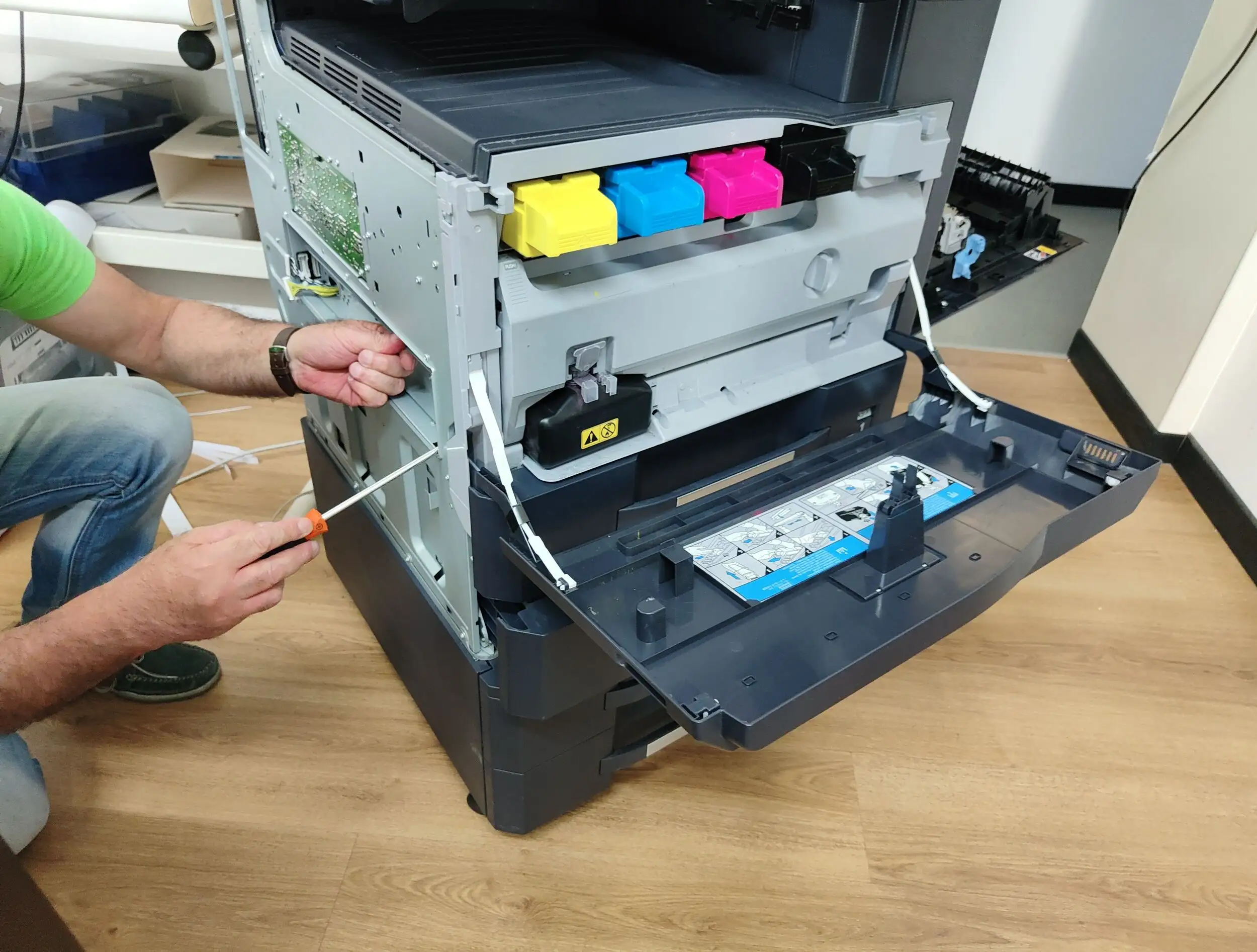 A man unscrewing a bolt on the side of the laser printer.