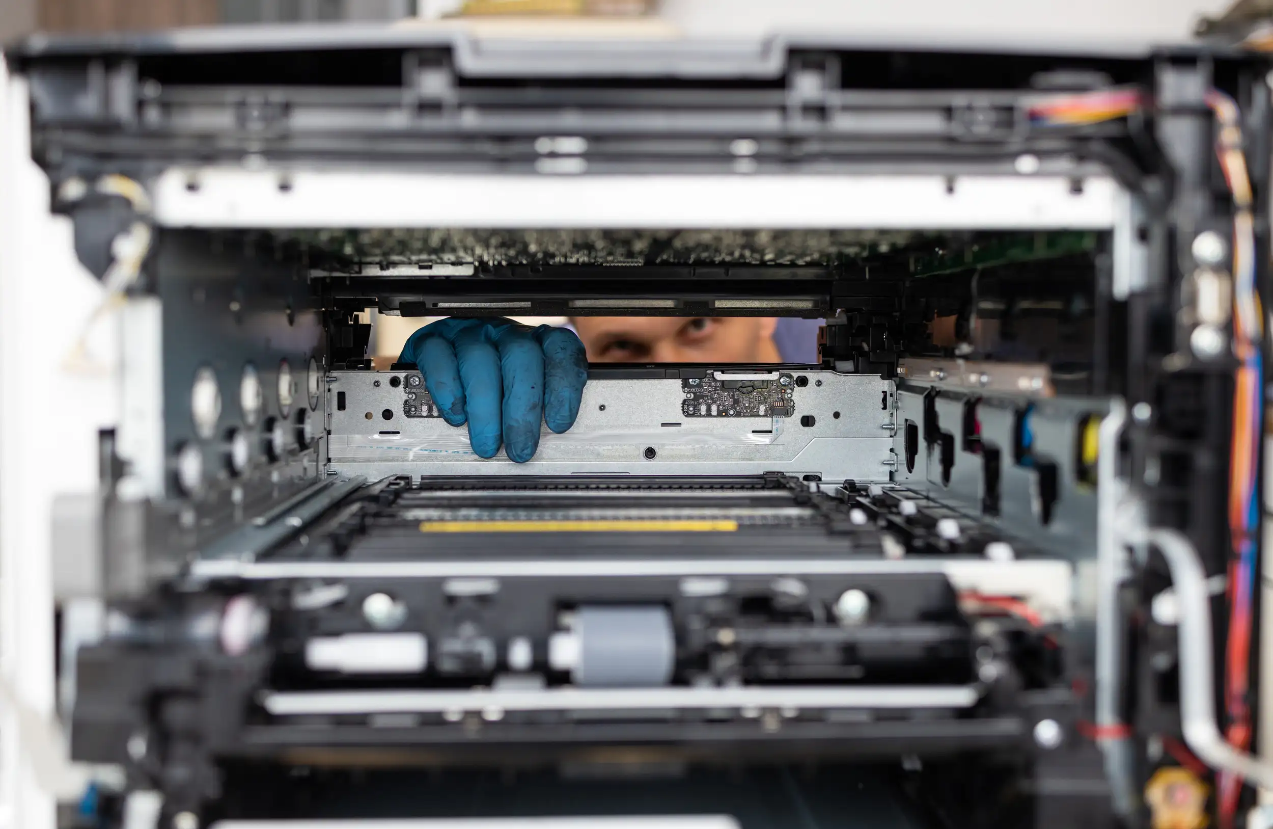 A close up look of the inside of a digital printer with a technician checking in the background.